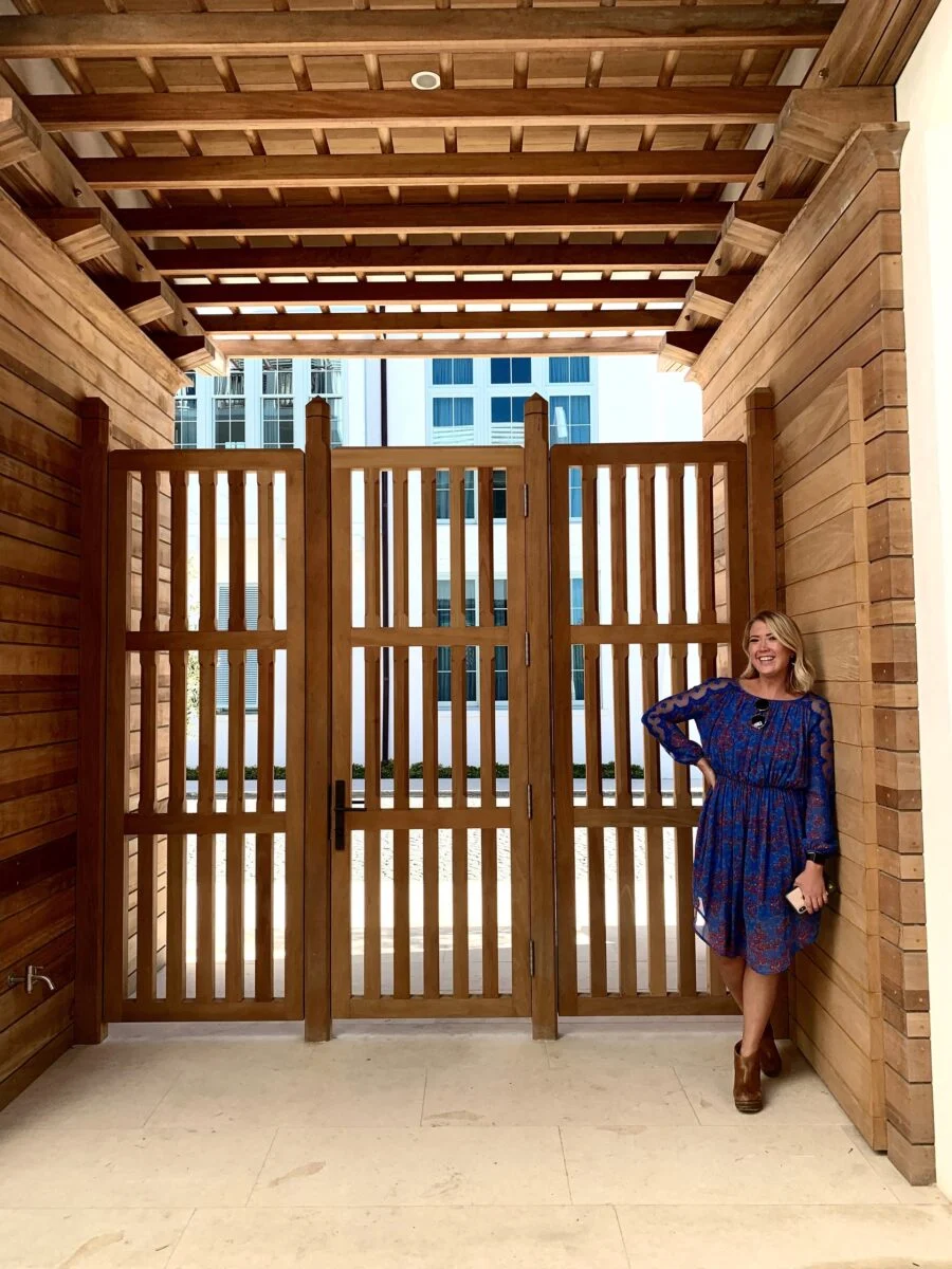 Custom Entry Gates – E. F. San Juan Woman standing in Alys Beach entryway gate with beautiful custom millwork by E. F. San Juan